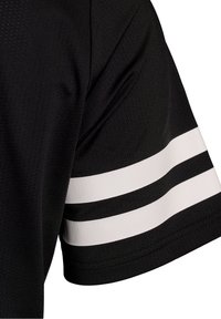Section de chemise noire à manches courtes avec deux bandes blanches horizontales près de l’ourlet de la manche, montrant la texture du tissu et les détails de couture.
