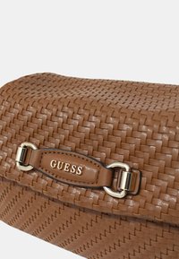 Borsa in finta pelle marrone intrecciata con superficie liscia, dettagli in metallo dorato e tracolla con logo impresso. Forma rettangolare compatta.