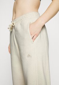 Pantalones de chándal beige claro hechos de suave algodón, con una cinturilla con cordón, bolsillos laterales y un logotipo bordado de Adidas.