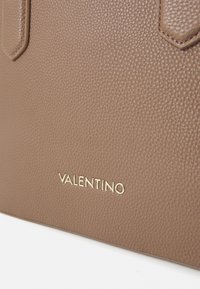 Borsa in pelle marrone con finitura a grana, caratterizzata dal logo "VALENTINO" in oro con un carattere moderno. Manici e design strutturato.