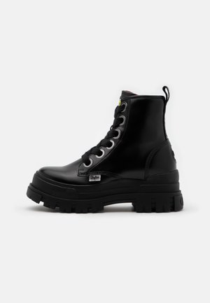 Botte montante noire en cuir à lacets avec semelle épaisse à crampons et languette au talon sur fond blanc uni.