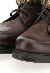 Brązowe skórzane buty z okrągłymi noskami, grubymi płaskimi podeszwami i teksturowanym wykończeniem. Udekorowane metalowymi ćwiekami wzdłuż góry.