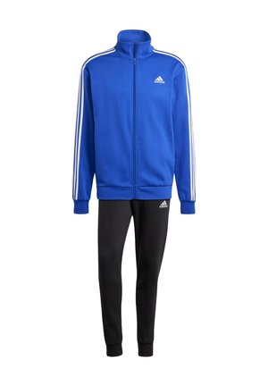 Modrá sportovní bunda na zip s bílými pruhy na ramenou, černé sportovní kalhoty. Materiál vypadá měkký, navržený pro pohodlí a pohyb.