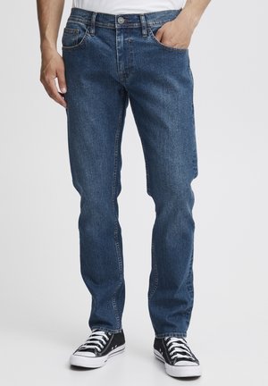 Blå denimjeans med rette ben, fem-lommers stil og sydd aksenter. Brukt med svarte sneakers og en enkel hvit skjorte.