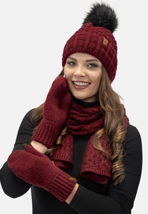 Cappello lavorato a maglia bordeaux con pompon nero, sciarpa abbinata e guanti con polsini a costine. Texture morbida con un motivo intrecciato.