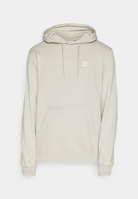 Světle béžová mikina Adidas s přední kapsou, nastavitelnou kapucí na šňůrku a bílým logem Adidas na levém hrudníku.