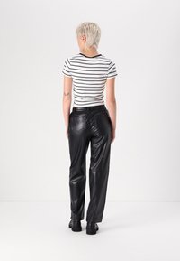 Calças de couro pretas com uma textura suave, combinadas com uma t-shirt justa às riscas brancas e pretas. Bolsos traseiros visíveis e design de perna reta.