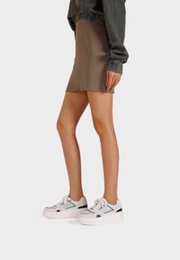 Mini gonna marrone a coste abbinata a sneaker bianche con dettagli blu e riflettenti. Le sneakers presentano un design con suola spessa.