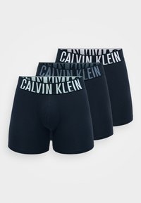 Három pár sötétkék boksznadrág elasztikus derékrésszel, amelyen a "CALVIN KLEIN" márkaneve kontrasztos színekben szerepel. Simás pamut anyag.