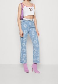 Witte cropped tanktop met roze rand en geborduurde vlinders, gecombineerd met lichtblauwe flared jeans met witte bloemenpatronen. Roze haklaarzen.