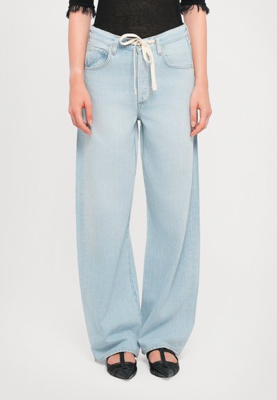 Lichtblauwe wijde jeans met een trekkoord in de taille, voorzien van zijzakken en een zachte denimtextuur. Gepaard met zwarte schoenen.
