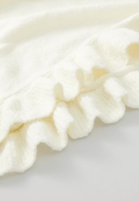 Kreemikakseline kudum, millel on pehme tekstuur ja laineline ripsdetail ääres, mis näitab vaikselt sügavust ja mõõtmeid.