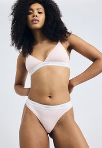 Light pink triangle bralette and matching bikini briefs with white elastic bands bearing the "HUGO" logo. Smooth fabric texture.