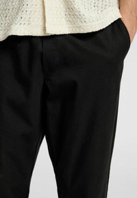 Czarne spodnie wykonane z gładkiego materiału, o prostym kroju nogawek i bocznych kieszeniach. Noszone z fakturowaną bluzką w kolorze kremowym.