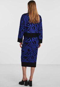 Modré šaty s geometrickými vzory, černé ozdoby na rukávech a lemu. Hladká látka, silueta přiléhající na postavu, délka ke kotníkům.