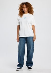 White cotton t-shirt with short sleeves and a colorful graphic on the chest, paired with loose blue denim jeans and black sneakers.