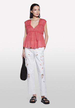 Top peplum in corallo con maniche a cap, abbinato a pantaloni bianchi con ritagli ricamati. Una borsa nera intrecciata e sandali neri chunky completano l'outfit.