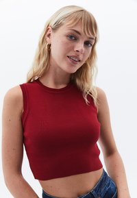 Červený žebrovaný crop top s kulatým výstřihem a bezrukávovým designem, s hladkou texturou a přiléhavým střihem.