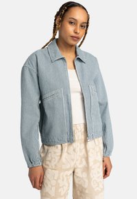 Striped blue jacket with a collar, two front pockets, elastic cuffs, and a zip closure, paired with beige patterned pants.