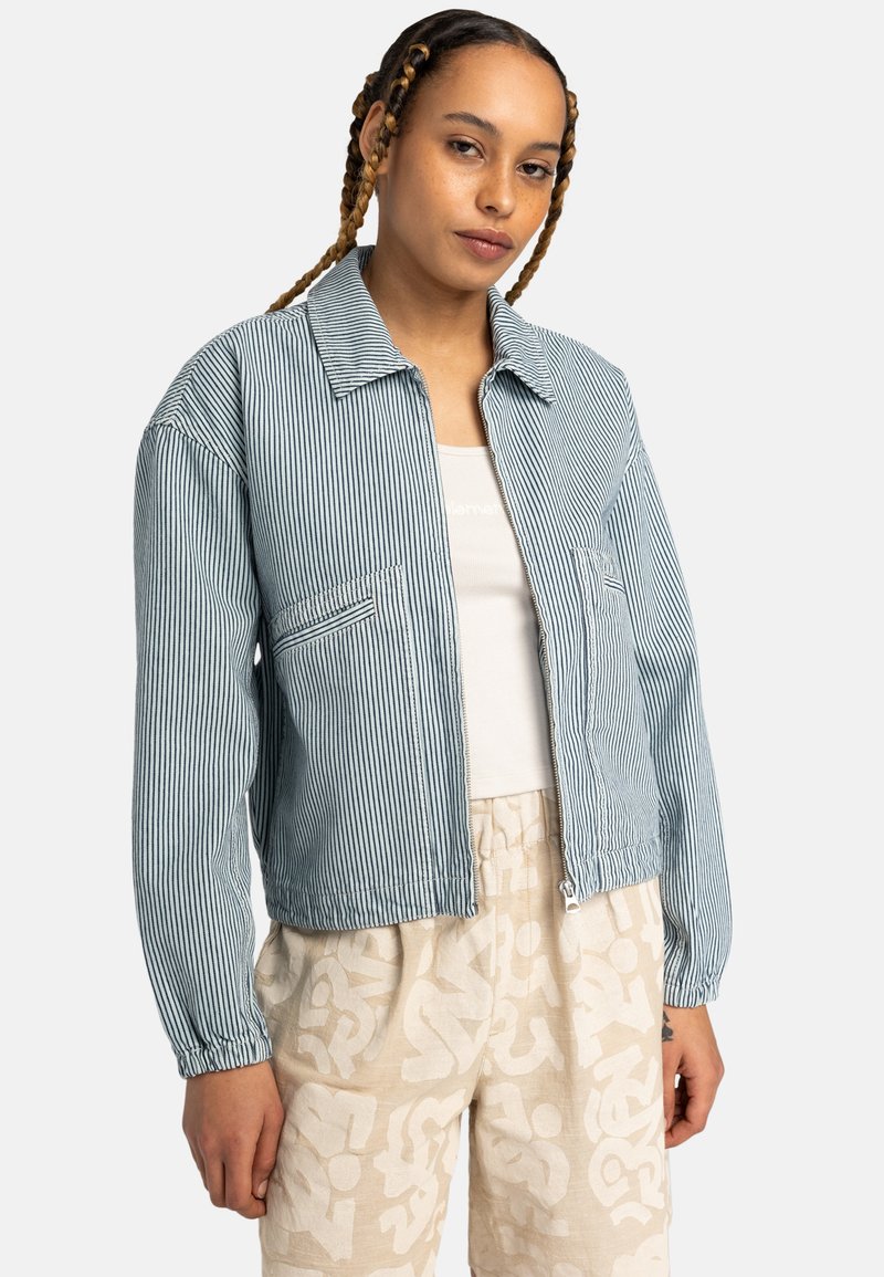 Striped blue jacket with a collar, two front pockets, elastic cuffs, and a zip closure, paired with beige patterned pants.