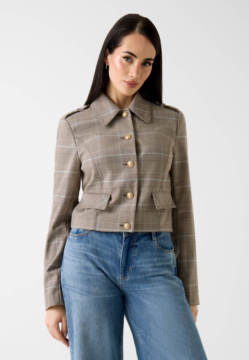 Veste courte à carreaux beige et marron, dotée de boutons dorés, d'un col pointu et de poches avant. Portée avec un jean large bleu clair.