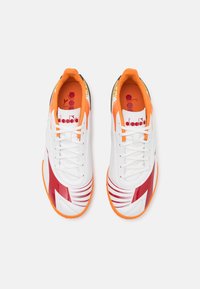 Zapatillas deportivas blancas con acentos en rojo y naranja, superiores sintéticas, con detalles texturizados y suela de goma plana, que presentan elementos de marca.