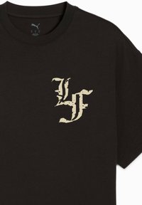 Sort bomulds t-shirt med korte ærmer, med et slidte beige logo-design på venstre bryst. Rund halsudskæring, standard pasform.