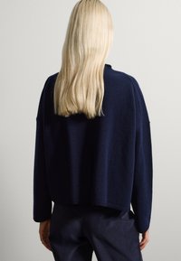 Suéter oversized de color azul marino con un acabado texturizado, hombros caídos y puños acanalados. Diseño minimalista, visto desde la parte posterior.