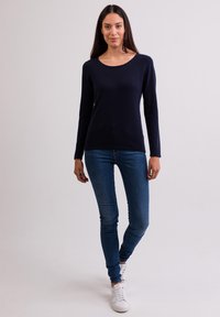 Granatowa, długorzędowa bluzka z dzianiny z okrągłym dekoltem, zestawiona z dopasowanymi niebieskimi dżinsami i białymi sneakersami, tworząc swobodny wygląd.