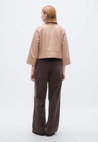 Rudos odos trumpa striukė su ribbinge apačioje, derinama su laisvomis rudomis kelnėmis. Nugaroje matoma lygi tekstūra ir minimalistinio dizaino detalės.