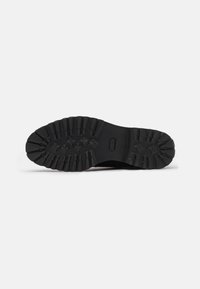 Semelle de chaussure en caoutchouc noir avec des rainures profondes, présentant une section centrale lisse et des motifs texturés pour une meilleure adhérence et traction.