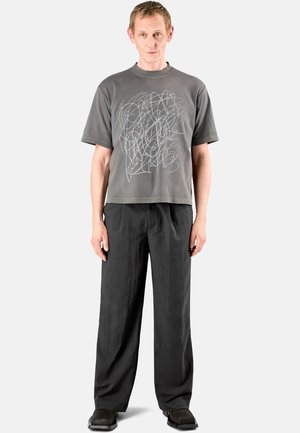 Szary T-shirt z abstrakcyjną białą grafiką, połączony z luźnymi czarnymi spodniami i płaskimi czarnymi butami. Prosty, swobodny design i fason.