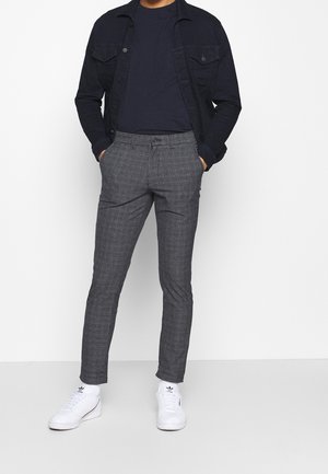 Šedé kostičkované kalhoty se slim fit střihem, zkombinované s tmavě modrou džínovou bundou a námořnickým tričkem, doplněné bílými teniskami.
