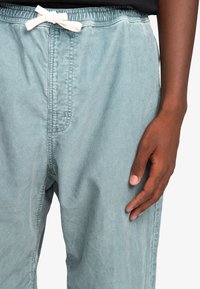 Light blue corduroy pants with an elastic waistband and a white drawstring. Close-up of fabric texture and stitching details.