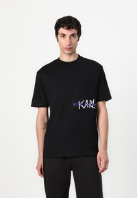 Fekete pamut póló, kék és fehér nyomott logóval a bal oldalon. Kerek nyakú, rövid ujjú, normál fazon.