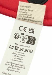 Red textile label with care instructions and symbols. Material: 100% organic cotton. Includes style, batch number, and compliance markings.