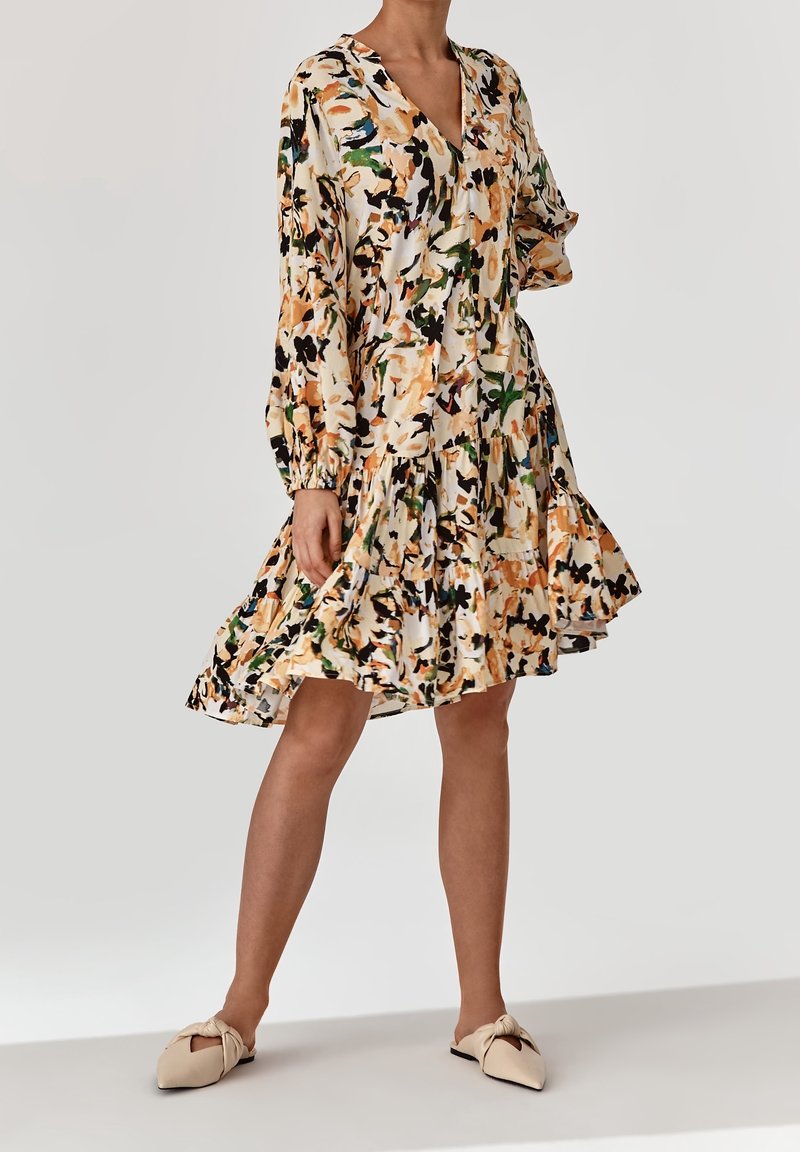 Vestido de estampado floral con mangas largas, escote en V y dobladillo en capas. La tela presenta colores de crema, naranja, verde y negro.