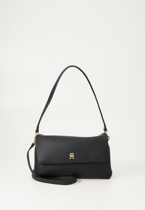 Black shoulder bag in smooth material, featuring a fold-over flap and gold logo accent. Adjustable strap for versatility.