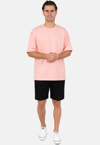 T-shirt di cotone rosa chiaro con maniche corte, abbinato a pantaloni corti neri. Il look è completato da sneakers bianche con dettagli rossi.