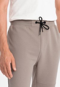 Béžové žebrované tepláky s pružným pasem a šňůrkou, s černými akcenty, bočními kapsami a texturovanou látkou.