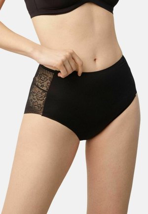 Mujer vistiendo ropa interior negra de cintura alta con paneles laterales de encaje floral, ajustando la cintura con su mano izquierda.