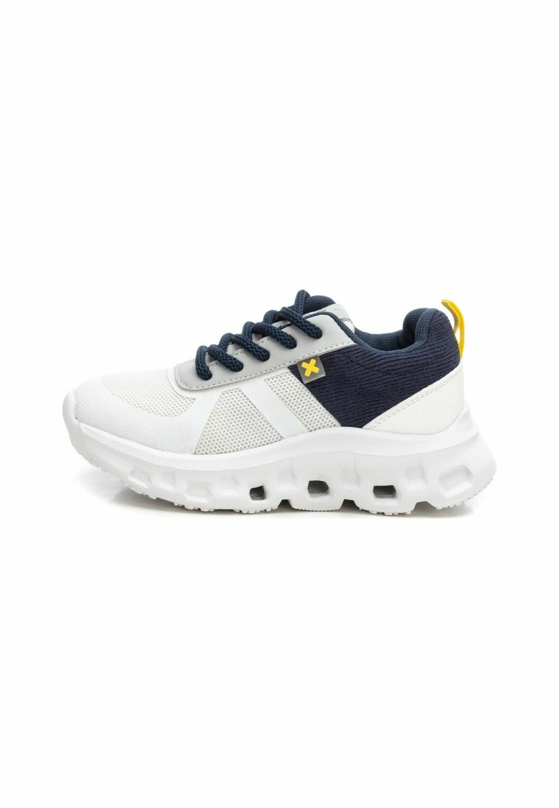 Zapatilla deportiva blanca con acentos de tela azul marino, parte superior de malla, suela de goma texturizada y bucle en el talón amarillo. Presenta cordones e inserciones elásticas.