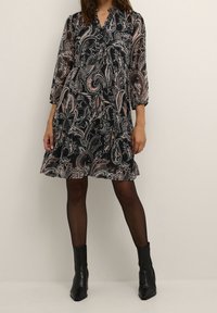 Black and cream paisley dress with long sleeves, a v-neckline, cinched waist, and a flared skirt. Paired with black ankle boots.
