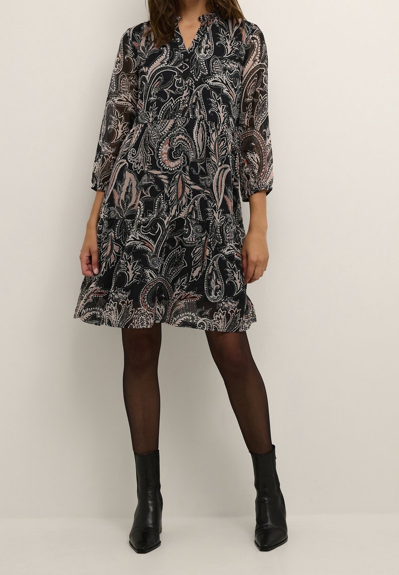 Black and cream paisley dress with long sleeves, a v-neckline, cinched waist, and a flared skirt. Paired with black ankle boots.
