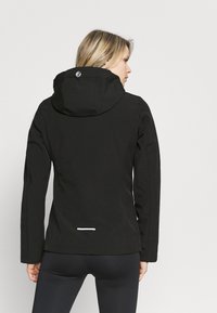 Zwarte waterdichte jas met capuchon, met een logo op de achterkant, rechte snit en reflecterend accent aan de onderkant. Glad stoffen textuur.