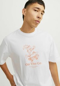 Witte katoenen t-shirt met een roze grafiek van een cartoonfiguur op een skateboard met de tekst "On The Go" eronder.