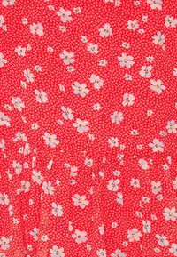 Tessuto rosso con una stampa floreale in piccolo bianco e rosa, caratterizzato da uno sfondo testurizzato. Il design include pieghe arricciate per un dettaglio aggiuntivo.