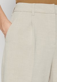 Beige, szabott nadrág sima textúrával, oldalsó zsebekkel és lapos elülső résszel. A derékszíj enyhén megemelt, letisztult kivitelben.