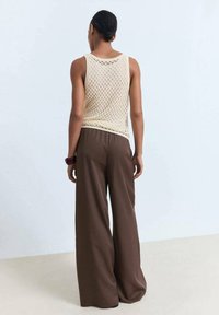 Jasno beżowy dzianinowy top na ramiączkach o luźnym kroju, połączony z szerokimi, brązowymi spodniami. Gładka tekstura i otwarty splot.