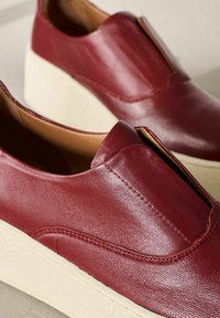 Czerwone skórzane pantofle wsuwane z podwyższoną beżową podeszwą, charakteryzujące się gładką teksturą i minimalnymi detalami przeszyć. Ergonomiczny design zapewniający komfort.